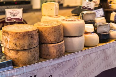 Milan, İtalya 27 Ekim 2025: Esnaf pecorino ve diğer geleneksel İtalyan peynirleri kırsal bir pazarda sergileniyor, taze tekerlekler ve takozlar satılık.