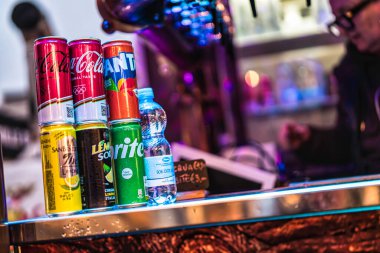 Milan, İtalya 27 Ekim 2025: çeşitli markalı soda kutuları ve plastik bir su şişesi neon ışıklı bir tezgahın üzerine dizilmiş, susuz müşterilere servis yapmaya hazır.