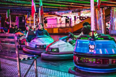 Milan, İtalya 27 Ekim 2025: konuklar renkli neon ışıkları altında neşeli bir gece panayırında gülerek ve çarpışan arabaları sürüyorlar.