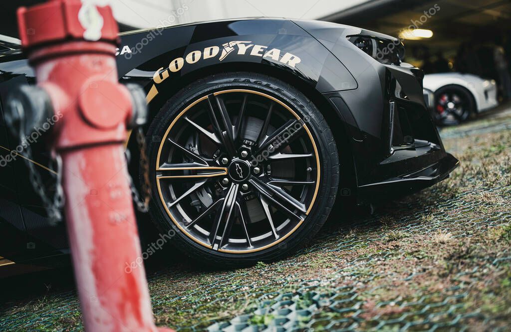 Milan, italy 28 october 2025: black chevrolet camaro wheel with goodyear tire and yellow stripe, parked beside a red fire hydrant on permeable paving