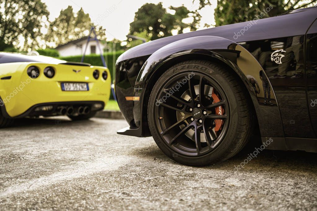 Milan, italy 28 october 2025: two iconic american muscle cars, a black challenger hellcat with red brake calipers and a yellow corvette, parked outdoors