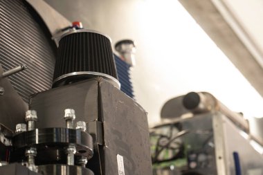 Karmaşık bir motor veya makineye bağlı hava filtresi, mekanik bileşenleri ve cıvatalar ve metal yapılarla endüstriyel çevreyi vurguluyor