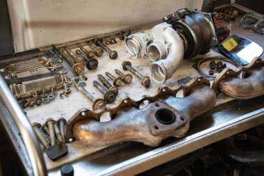 Kirli bir tezgahta duran yeni bir turbo şarj aleti ve eski egzoz manifoltları da dahil olmak üzere araba parçaları, bir otomobil garajında motor tamiri veya modernizasyon hizmeti için hazır.
