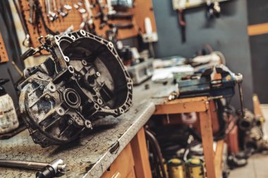 Parçalanmış araba vites kutusu konutları kirli bir atölye tezgahında arka planda bulanık tahta araçlar, otomotiv onarımı, bakım ve mekanik elden geçirme