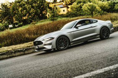 Vo, italyan 28 Ekim 2025: Gümüş Ford Mustang kaslı araba dolambaçlı bir köy yolunda parçalanmış, güneşli krom ve açık yol özgürlüğünü yakalayan güçlü hareket