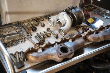 Roma, İtalya, 20 Kasım 2025: motor tamiri sırasında araba parçaları bir arabanın üzerinde duruyor, eski egzoz manifoltlarını gösteriyor, cıvataları bağlıyor, ve yeni bir turbo-şarj aleti.