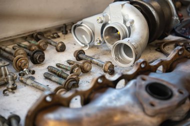 Roma, İtalya, 20 Kasım 2025: motor parçaları, yeni bir turbo şarj aleti ve eski egzoz manifoldu dahil, bir otomotiv atölyesinde kirli bir tezgahta dinleniyor.