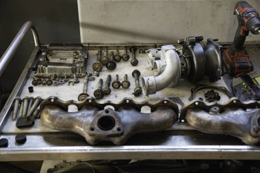 Roma, İtalya, 20 Kasım 2025: sökülmüş turbo şarj aleti, egzoz manifoltları, civatalar ve araba motor parçaları onarım ve bakım için metal bir sepetin içinde düzenlendi.