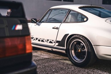 Vo, İtalya 28 Ekim 2025: Beyaz Porsche 911 Carrera ve siyah BMW asfalt üzerinde yan yana park edilmiş, klasik tarzda sergileniyor, Alman mühendisliği ve performansı