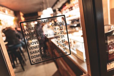 Rovigo, İtalya, 18 Aralık 2025: İtalyan pastanesi bir cam kapı üzerinde günlük açılış ve kapanış saatlerini gösteriyor, müşterilere önemli bilgiler sunuyor