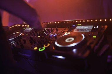 Rovigo, İtalya, 18 Aralık 2025: Dj canlı kırmızı ve yeşil ışıklar altında profesyonel ses ekipmanlarını karıştırıyor, eller mikserde enerjik gece kulübü atmosferi yaratıyor.