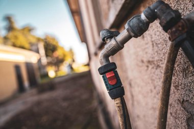 Bahçe musluğu ve hortum bağlantısı sert beton duvara monte edilmiş. Metal musluk ve adaptörün yakın çekim detayları arka bahçedeki su ve dış bakım için hazır.