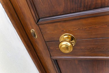 Parlatılmış pirinç kapı tokmağı ve ahşap bir kapının görünür kilidi, ev, güvenlik, mahremiyet ve klasik bir konut ortamının giriş ve çıkışını çağrıştıran yakın plan detay