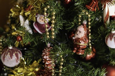 Noel ağacı dalları çeşitli kırmızı ve beyaz süsler, ışıltılı süsler, altın boncuklar ve Noel Baba figürleri taşıyarak, geleneksel ve geleneksel bir tatil atmosferi yaratıyor.