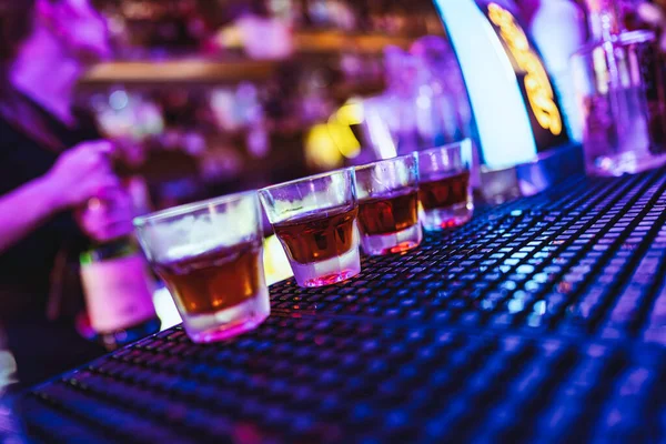 Barmen alkolle dolu bir sıra içki bardağıyla neon ışıklı bir gece kulübünde içki hazırlıyor. Islak bar tezgahında oturmuş, kutlamaya ve eğlenmeye hazır.