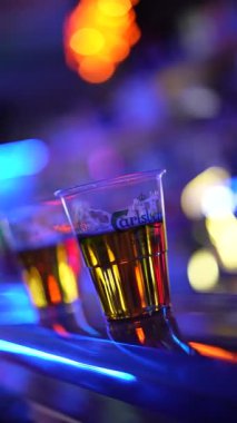 Roma, İtalya, 2 Ocak 2026: Bir müzik festivalinde plastik bardaklarda soğuk bira. Sahnenin parlak neon ışıkları ve bulanık, renkli bir arka planı var.