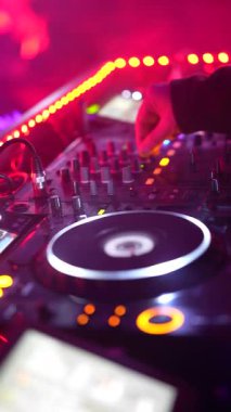 Roma, İtalya, 2 Ocak 2026: Bir DJ 'in ellerini bir mikser konsolunun kontrollerini ustalıkla manipüle ederek yakın plan partisi ışıkları altında döner.