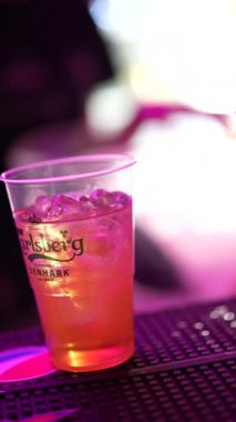 Roma, İtalya 2 Ocak 2026: profesyonel barmen canlandırıcı bir alkollü kokteyl hazırlıyor. Plastik bardakta, parlak pembe neon ışıkları olan bir tezgahta.