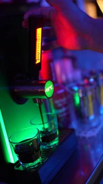 Roma, İtalya 2 Ocak 2026: Barmenin eli neon ışıkları olan bir gece kulübünde özel bir soğutma makinesinin bardağına jgermeister likörü döküyor..