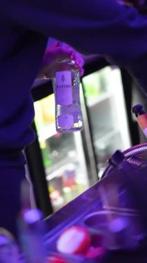 Roma, İtalya 2 Ocak 2026: profesyonel barmen bir gece kulübünde plastik bardakta alkollü bir kokteyl ile buzu karıştırıyor. Mor ve mavi neon ışıklar bar tezgahını aydınlatır