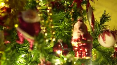 Noel Baba süslemeleri, parlak kırmızı mücevherler, altın boncuklar ve ışıldayan sıcak peri ışıklarıyla süslenmiş bir Noel ağacının detaylı görüntüleri neşeli ve rahat bir tatil atmosferi yaratıyor.