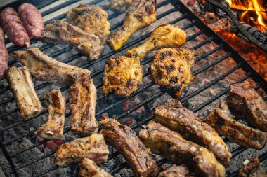 Domuz kaburgası, tavuk parçaları ve sosisler dahil çeşitli etler görünür duman ve alevlerle sıcak kömürün üzerinde ızgara yapmak ve lezzetli bir açık hava yemeği hazırlamak.
