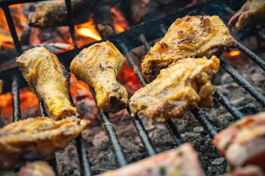 Tavuk budu ve kanatları metal ızgarada cızırdıyor. Parlayan kömür ve alevler üzerinde ızgara yapıyor. Altın kahverengi ve dumanlı.