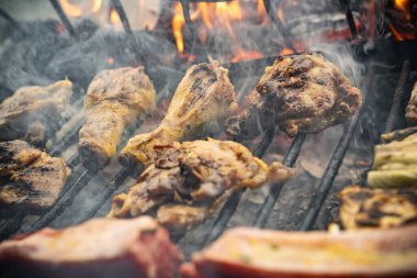 Sıcak ızgarada pişen tavuk parçaları dumanın yükseldiği ve alevlerin göründüğü ızgarada leziz bir açık hava yaz yemeği ve yemek deneyimini temsil ediyor.