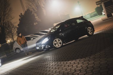 Roma, İtalya, 9 Ocak 2025: Siyah Opel Corsa Opc 'a bakan genç adam ve sisli sokak lambaları altında park etmiş arabalar gece vakti