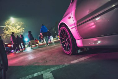 Roma, İtalya, 9 Ocak 2025: araba gece neon ışıklı bir otoparkta buluşuyor. Pembe ve mavi yansımalar özel arabalar, tekerlekler ve hayranlar bir araya geliyor..