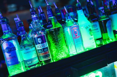 Roma, İtalya, 9 Ocak 2025: bir bar rafında çeşitli içki ve içki şişeleri, canlı yeşil ve mavi ışıklarla aydınlatılmış, gece hayatı atmosferi yaratıyor.