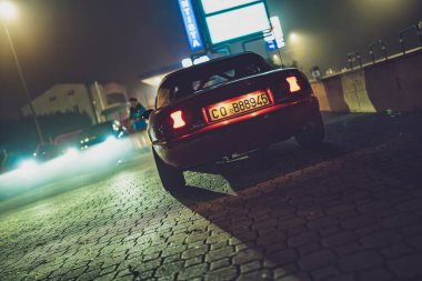 Roma, İtalya 9 Ocak 2025: Kırmızı mazda miata gece kaldırım taşı caddesinde park edilmiş, şehir ışıkları ve yakınındaki arabalar dengesiz, sinematik ortam yaratıyor.