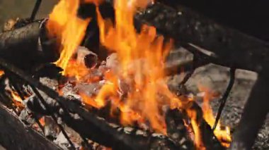 Yoğun turuncu ve sarı alevler, kömürleşmiş odunları ve yanan közleri bir ateş çukurunun içinde, parlak titreşimler ve dumanla sıcak, samimi ve büyüleyici bir doğal ekran yaratır.