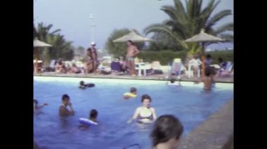 Mallorca, İspanya Haziran 1978: Otantik 8mm film, insanların güneşli bir günde yüzme havuzunda eğlendiklerini gösteriyor. Aileler ve arkadaşlar yüzüyor, oynuyor ve dinleniyor.