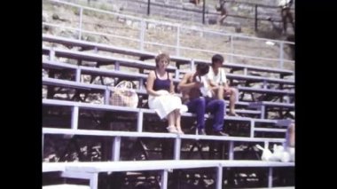 Palermo, İtalya, Haziran 1980: Stadyum tribünlerinde oturan bir kalabalığın orijinal 8 mm 'lik klasik görüntüleri. Seyirciler 1980 'lerin güneşli bir yaz gününde açık hava etkinliğini izliyorlar