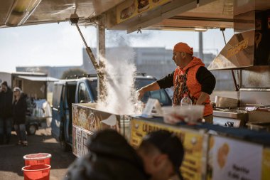 Imola, İtalya 01 Ocak 2026: Buharlı sokak yemekleri satan ve güneşli bir pazarda müşterileri meşgul eden adam.