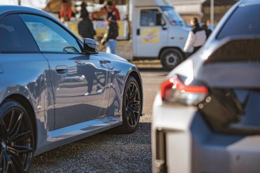 Imola, İtalya 01 Ocak 2026: Pürüzlü bir profil ve dinamik alaşımlı spor coupe açık hava araba fuarında bulanık kalabalık ve yemek kamyonu ile modern metalik spor coupe