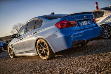 Imola, İtalya 01 Ocak 2026: karbon aksanlı mavi bmw m3 sedan, özel alaşımlı tekerlekler ve çakıl üzerine park edilmiş spor egzoz gün batımında, arka üç çeyrek manzara