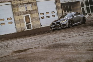 Imola, İtalya 01 Ocak 2026: endüstriyel depo kapılarından önce park etmiş gri BMW M2 coupe, gösterişli çizgiler, sportif duruş ve şehir otomotiv tasarımı