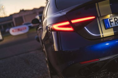 Imola, İtalya 01 Ocak 2026: Mavi alfa romeo giulia arka görüş, parlayan kuyruk lambası, altın yarış çizgileri, karbon fiber aksanlar ve alacakaranlıkta çift egzoz