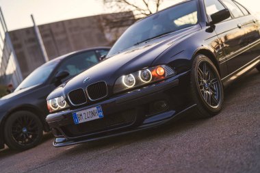 Imola, İtalya 01 Ocak 2026: asfalta park etmiş siyah bmw e39 sedan. Melek gözlü farlar aydınlatılmış, araba ayarlama ve otomotiv tarzının özünü yakalıyor.