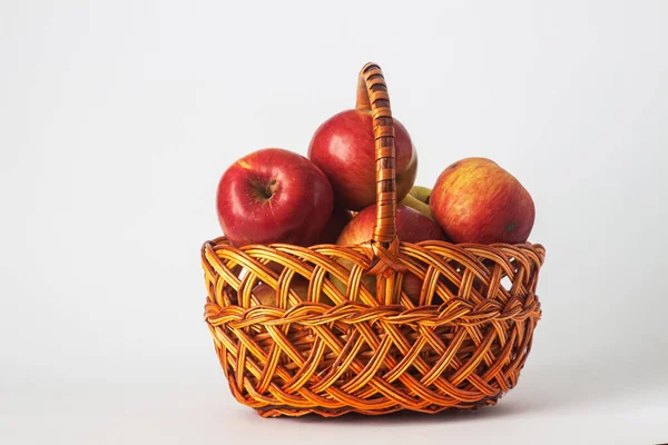 Beyaz bir arka planda el yapımı hasır bir sepette olgun elmalar. İzole bir hayat.