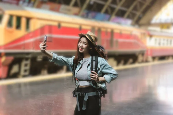 鉄道駅で写真や自撮りを撮るバックパック付きの陽気な若いアジアの女性旅行者 旅行ライフスタイルのコンセプト — ストック写真