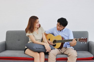 Mutlu genç Asyalı çift oturma odasında akustik gitar çalıyor. Tatlı, rahat, Romantik ve Aşk