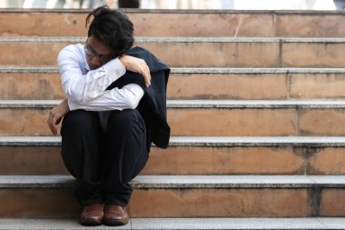 Depresyondaki takım elbiseli Asyalı genç iş adamı merdivenlerde ağır depresyondan muzdarip. İşsizlik ve işten çıkarma kavramı.