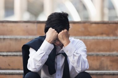 Endişeli genç Asyalı iş adamı ofis dışında oturuyor ve ağır depresyondan muzdarip. İşsizlik ve işten çıkarma kavramı.