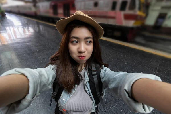 鉄道駅で写真や自撮りを撮るバックパック付きの陽気な若いアジアの女性旅行者 旅行ライフスタイルのコンセプト — ストック写真