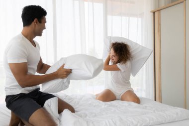 Yatak odasındaki yatakta yastık savaşıyla eğlenen mutlu genç çift. Zevk, Aşk, İlişki