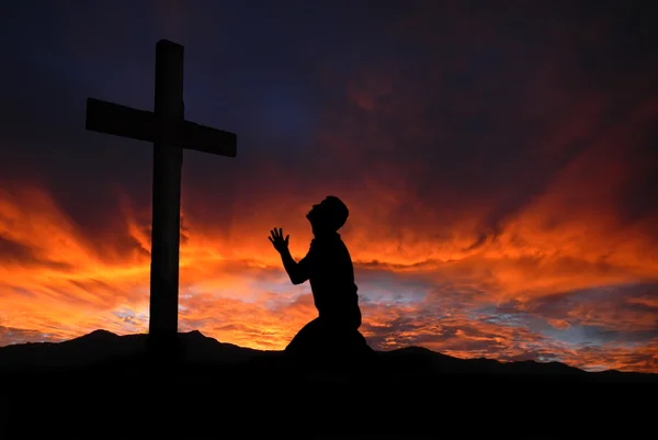 Silhueta de homem orando a uma cruz com céu cloudscape su — Fotografia de Stock