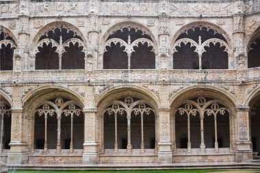 Lizbon 'daki Jeronimos Manastırı' nın zarif taş manastırı avlusunda süslü kemerler, Gotik ve Manueline mimarisi ve simetrik tarihi tasarım yer alıyor.